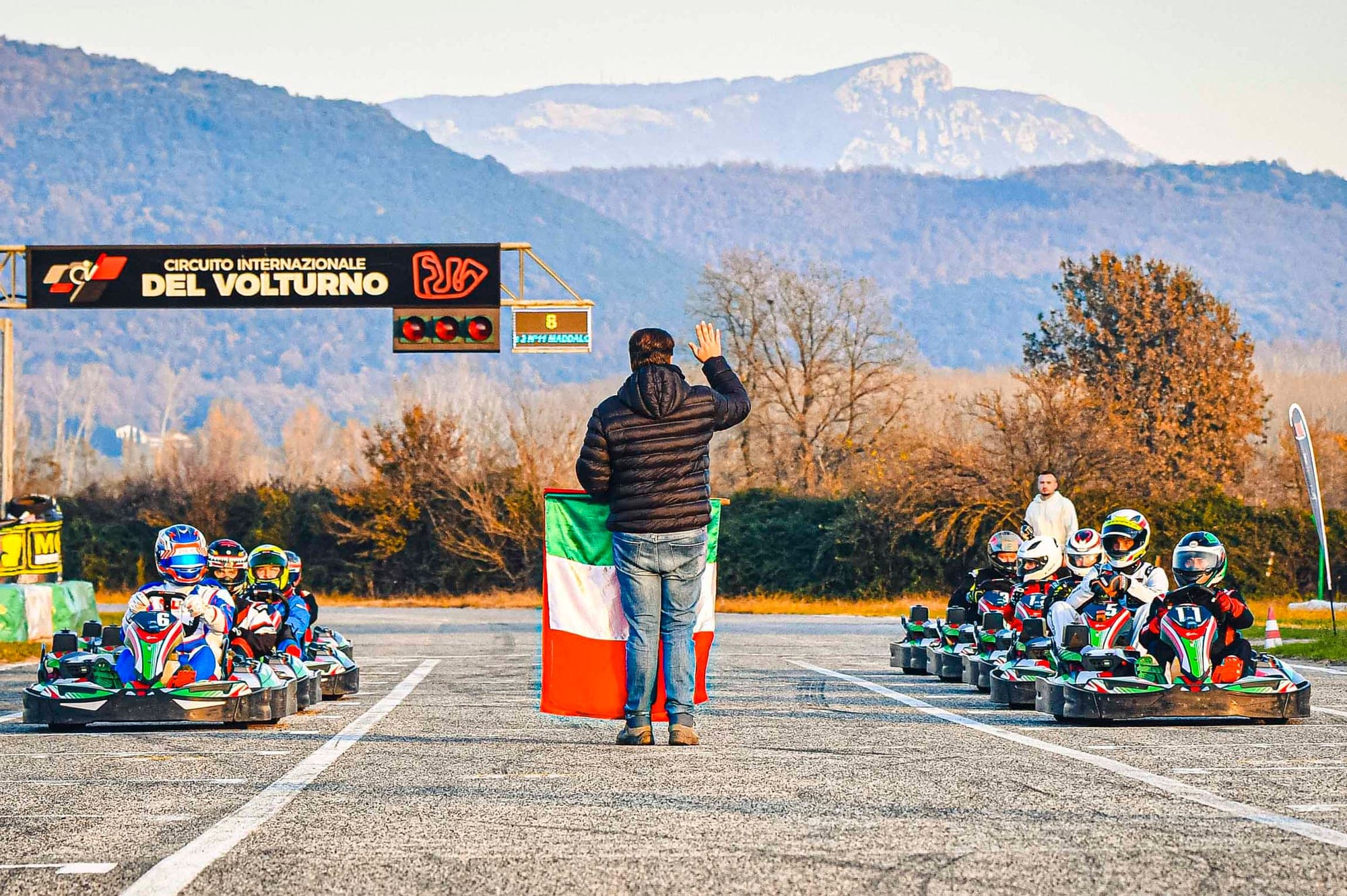 Partenza di una gara di kart sotto il portale del circuito, con la bandiera italiana